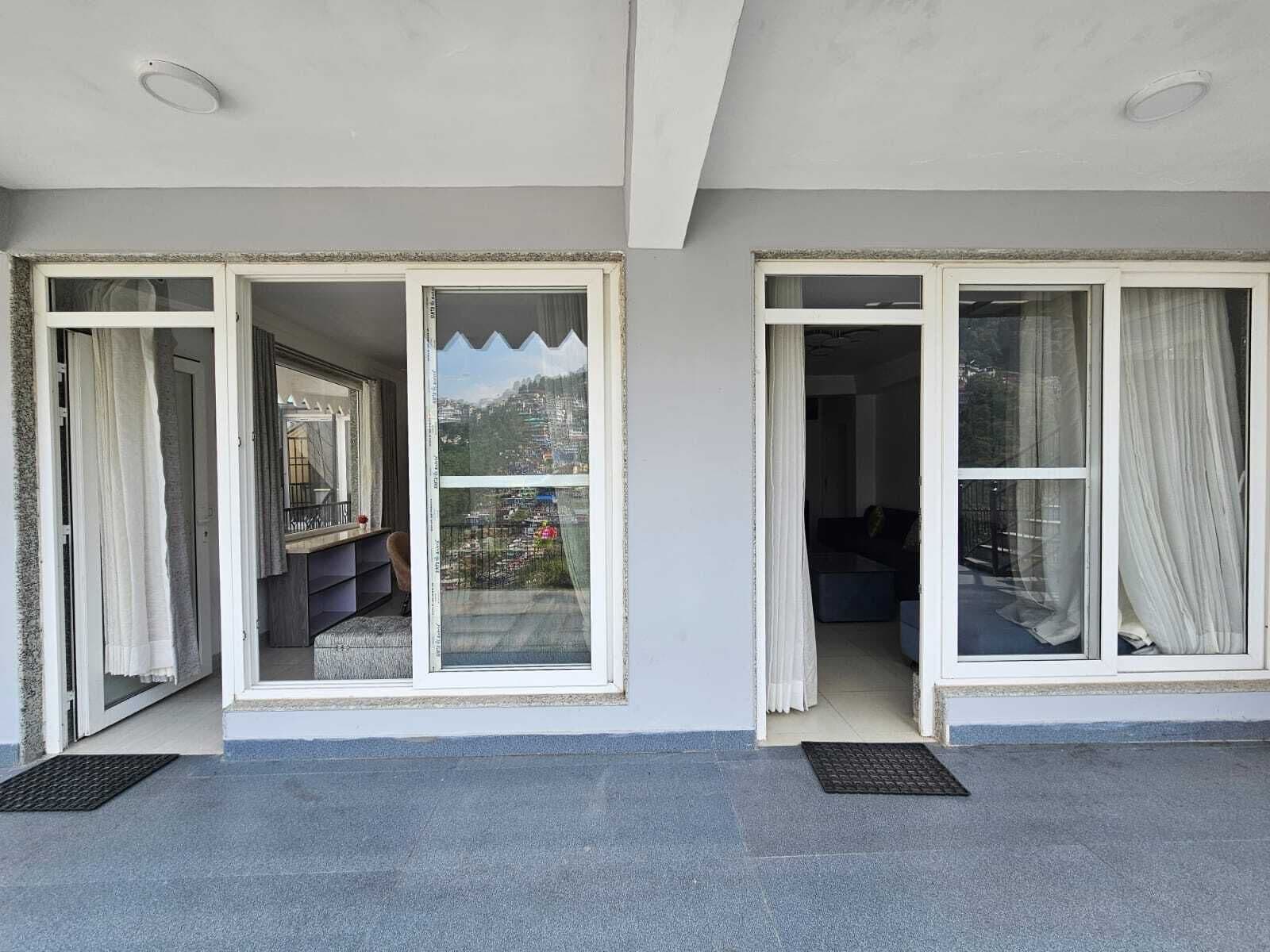 A modern building with large sliding glass doors leading to a balcony with a view of a mountainous landscape.