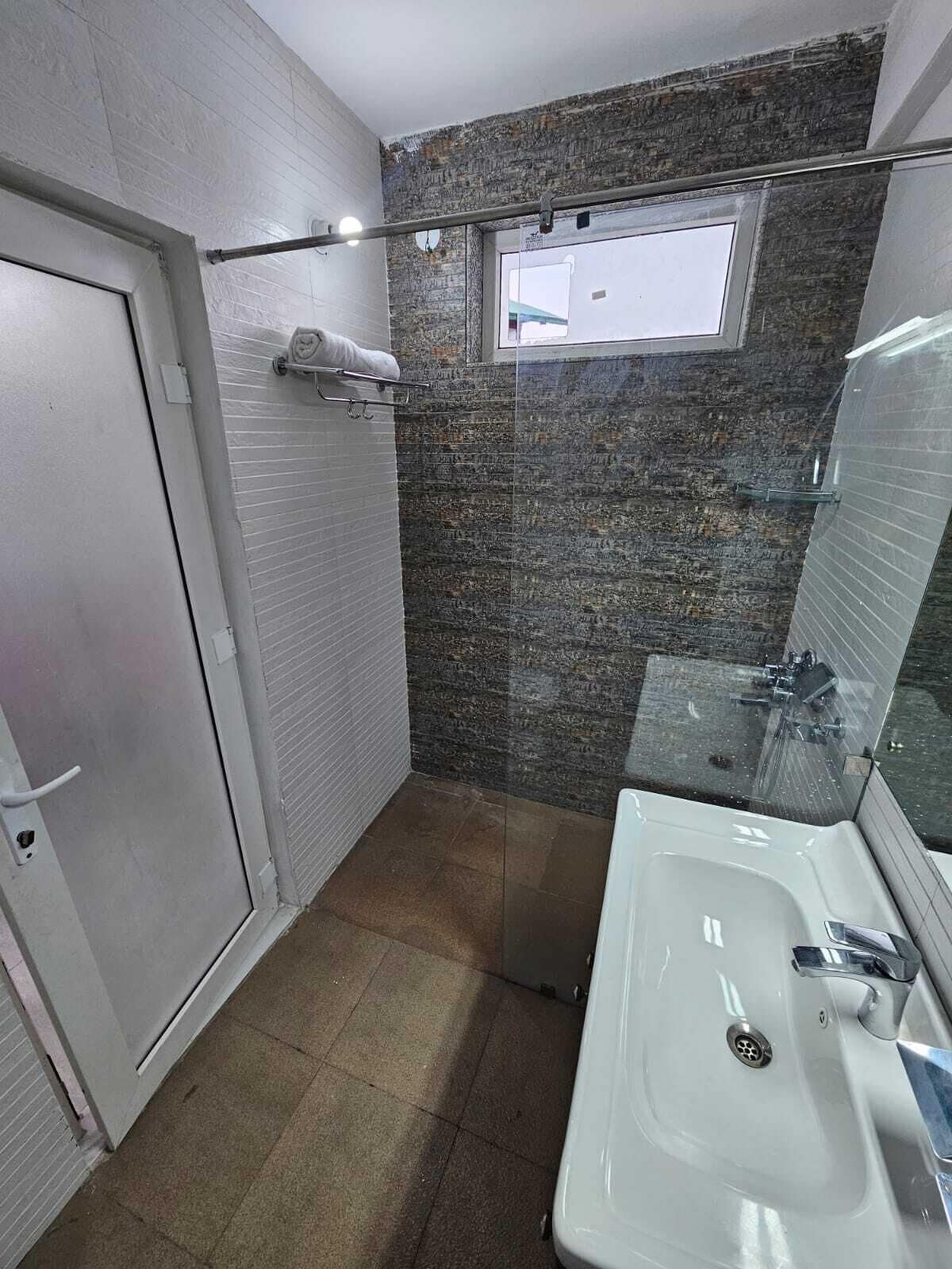 Een badkamer met een wit wastafelmeubel, een glazen douchecabine en een deur.