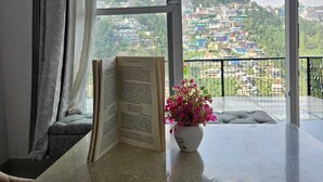 A room with a large window, a book, and a flower vase. - Sukon House by Crimson Horizon (Mussoorie)