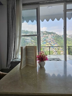 A room with a large window, a book, and a flower vase.
