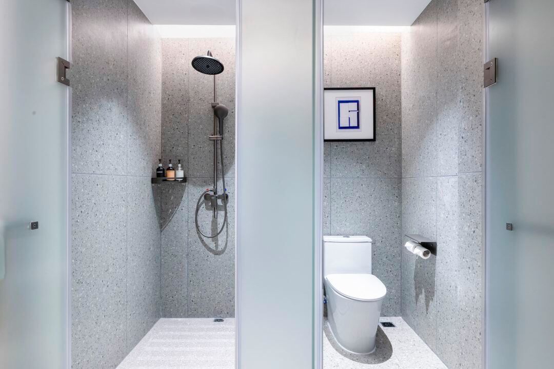 Un baño moderno con ducha, inodoro y un pequeño estante con artículos de aseo.
