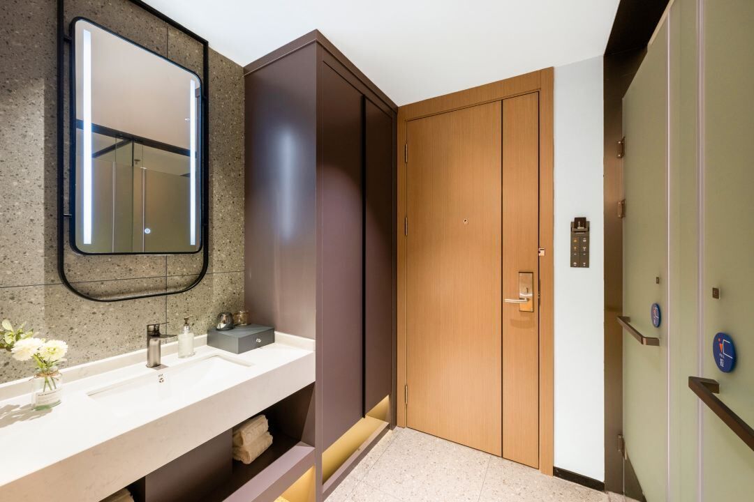 A modern bathroom with a large mirror, a sink, and a wooden door.