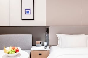 Quarto de hotel com cama, mesa de cabeceira com uma cesta de frutas, estação de carregamento e um quadro na parede.