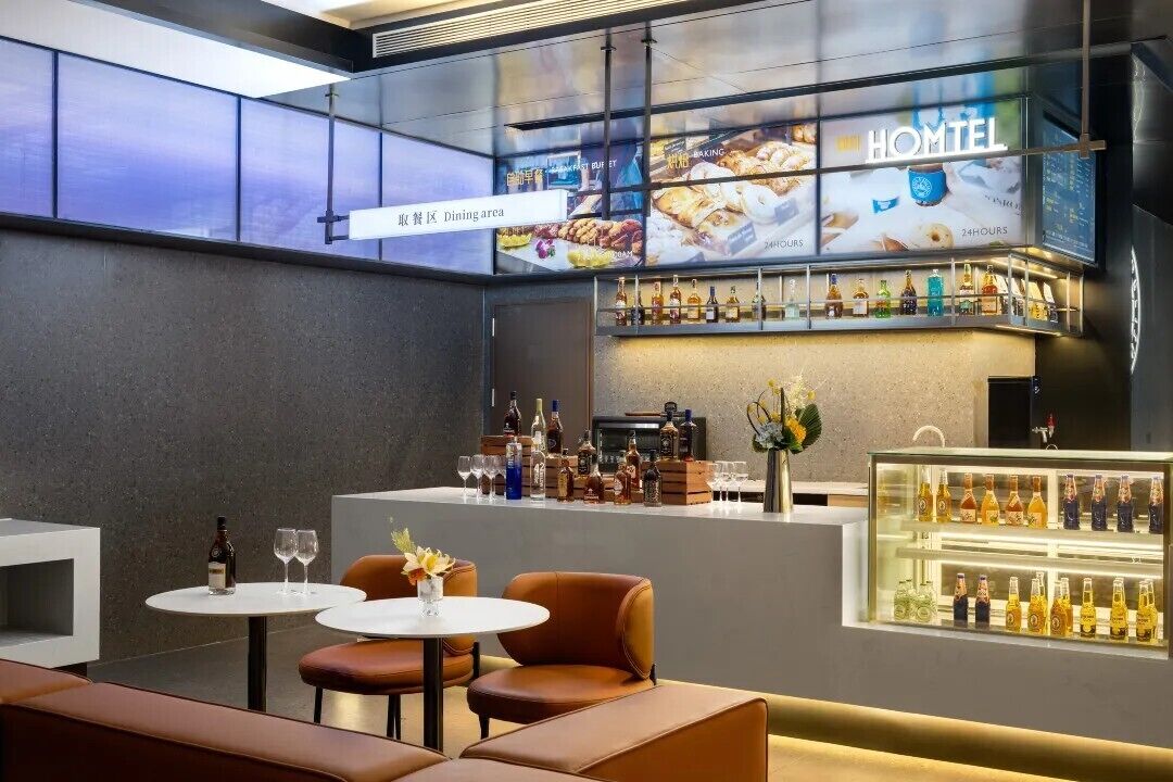 A modern bar area with a glass display case of bottles, seating with a view, and a digital menu board.