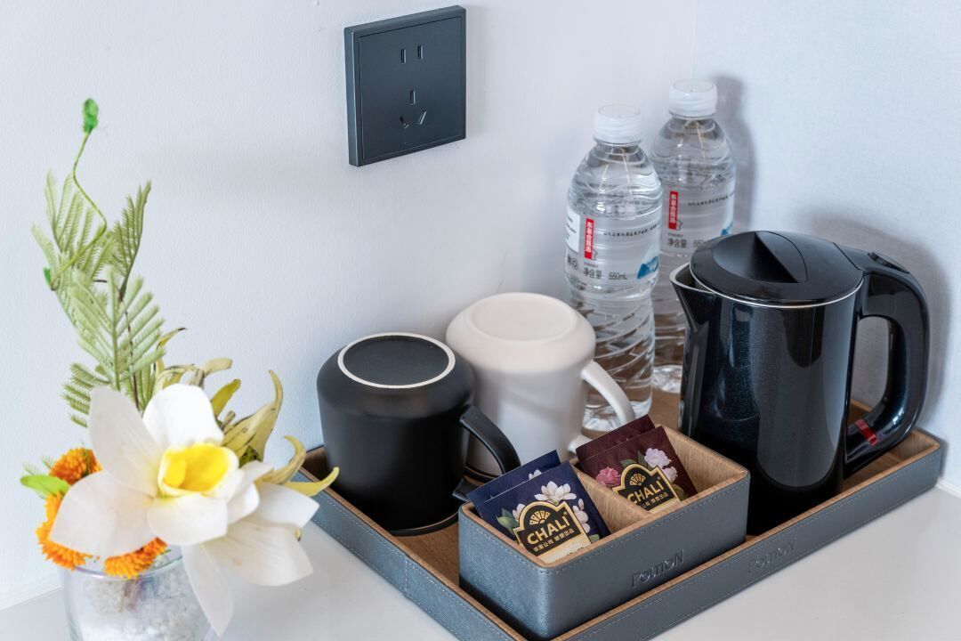 Una bandeja con una cafetera, dos tazas, una botella de agua y una caja de bolsitas de té chai.