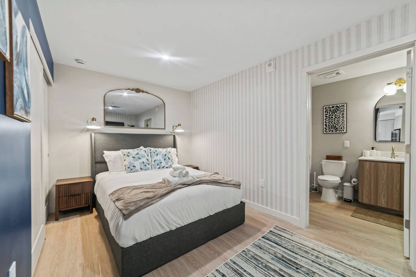 A modern bedroom with a large bed, bedside tables, a mirror, and a view into the bathroom.