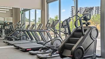 A row of treadmills in a gym with large windows and a view of buildings outside.