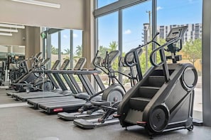 A row of treadmills in a gym with large windows and a view of buildings outside.