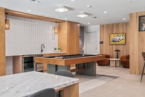 A modern kitchen with a pool table, wooden accents, and a dining area with a marble table.
