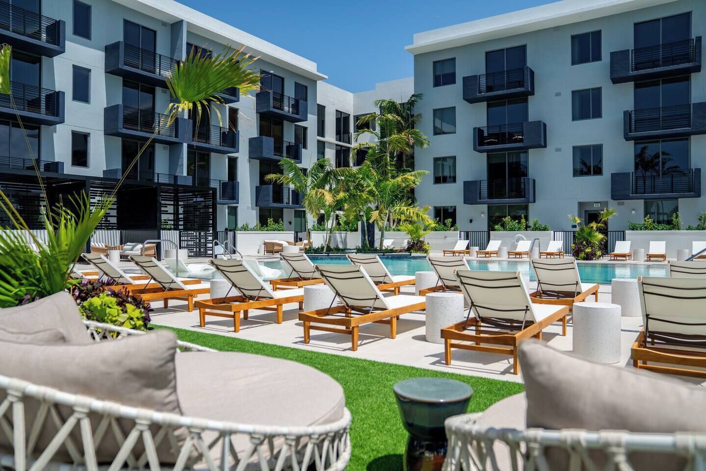 A poolside area with lounge chairs and a swimming pool, surrounded by a building with balconies.