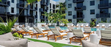 A poolside area with lounge chairs and a swimming pool, surrounded by a building with balconies.