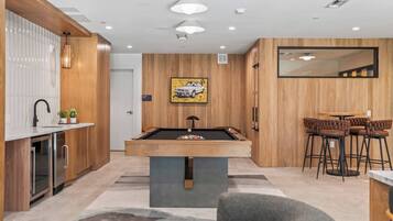 A modern kitchen with a pool table, bar stools, and a wooden accent wall.