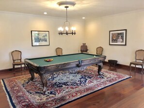 A pool table with a green felt surface, surrounded by a patterned rug, in a room with a chandelier and framed artwork on the walls. - Grand Craftsman Estate built in 1937 Charms in the heart of Carmel By The Sea (Carmel)
