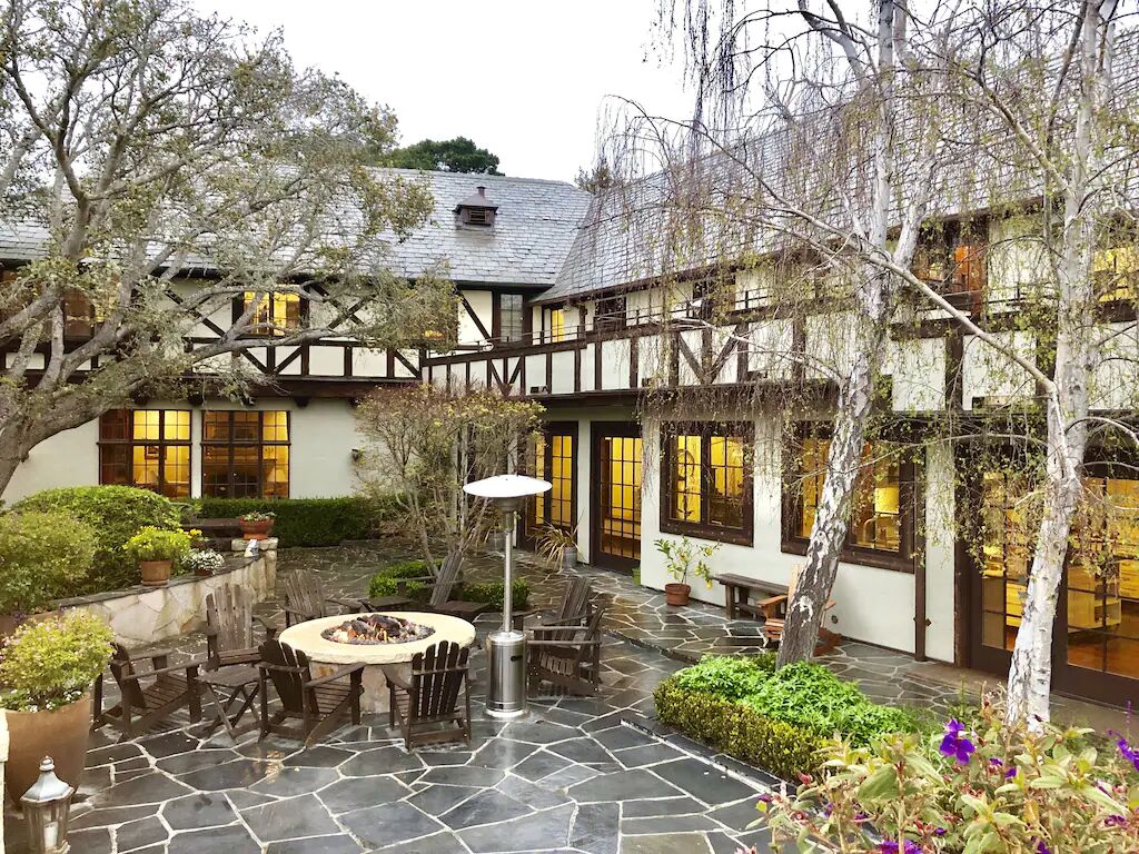 A courtyard with a stone fire pit, wooden furniture, and a view of a building with a Tudor-style facade.
