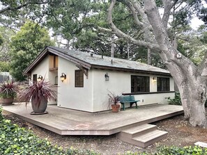 A single-story building with a sloped roof, a porch with a bench, and potted plants. - Grand Craftsman Estate built in 1937 Charms in the heart of Carmel By The Sea (Carmel)