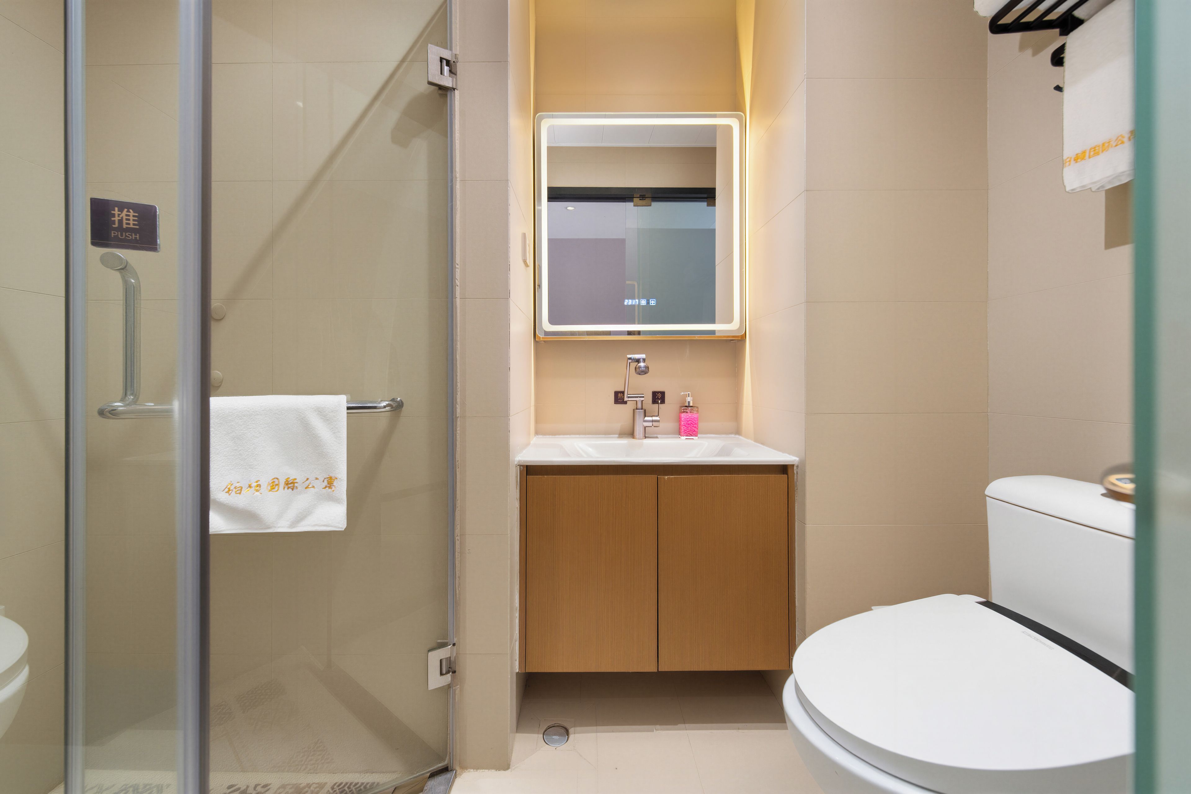 A modern bathroom with a glass shower enclosure, a white toilet, and a wooden vanity with a mirror above the sink.