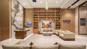 A hotel lobby with a reception desk, seating area, and a large wall-mounted television. - Poltton International Service Apartment (Foshan Yingtian Plaza Wanhua Metro Station (Foshan)