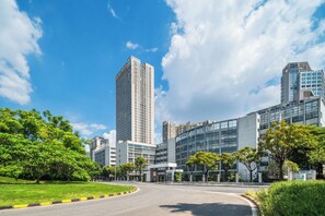 A modern building with a prominent tower, surrounded by greenery and a curved road. - Poltton International Service Apartment (Foshan Yingtian Plaza Wanhua Metro Station (Foshan)