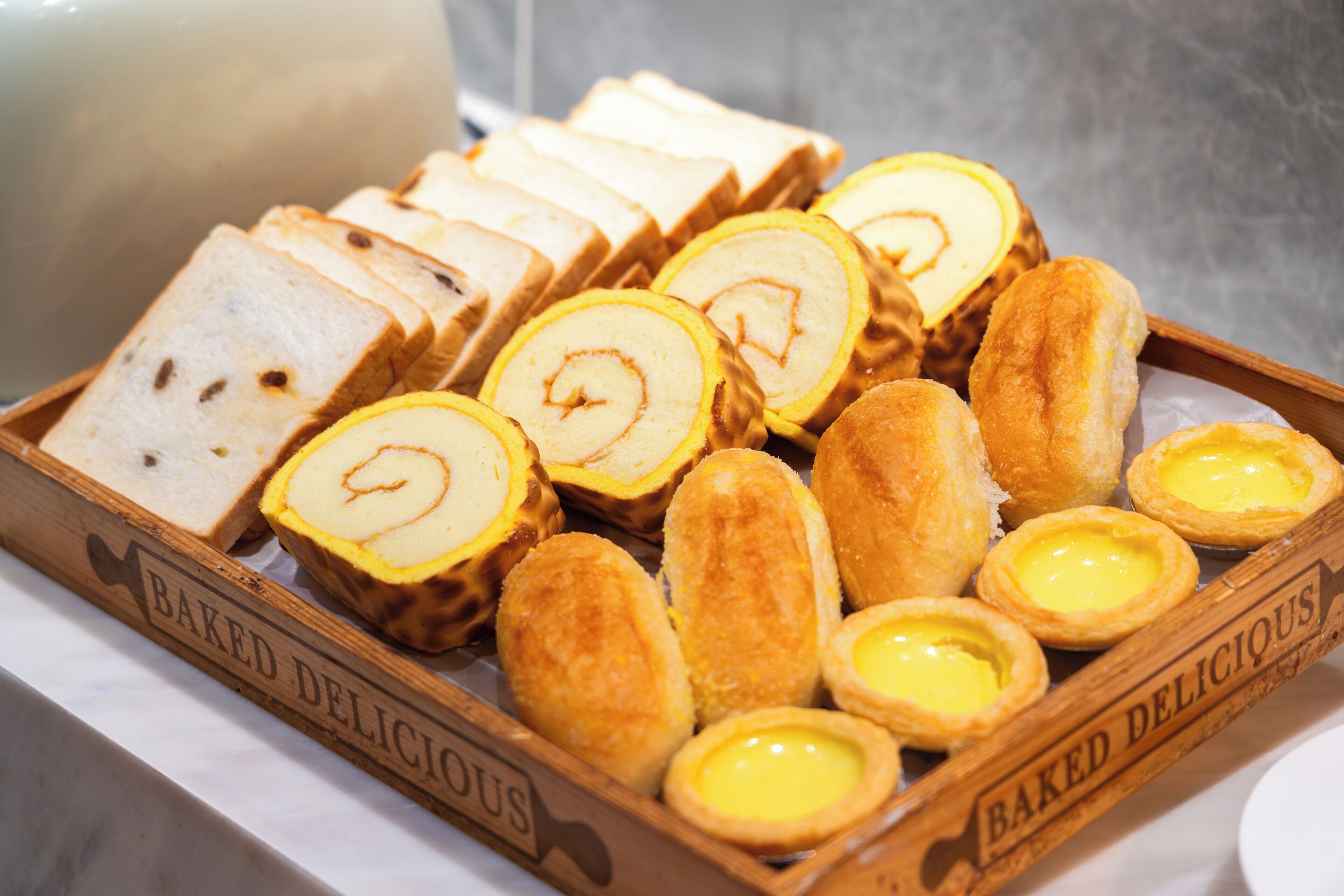 Un plateau en bois contenant divers produits de boulangerie, notamment du pain, des petits pains et des tartes.