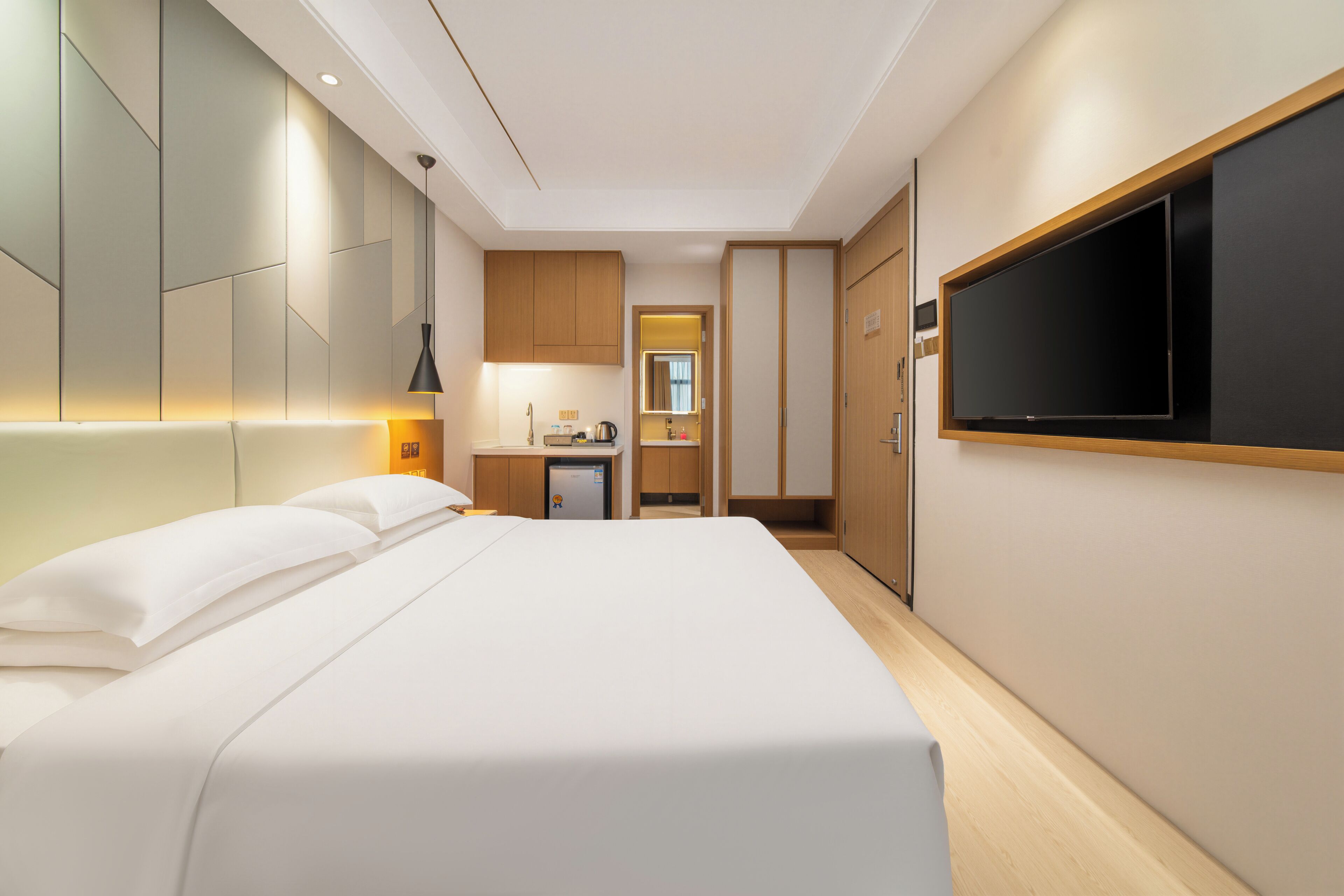 Ett modernt hotellrum med en stor säng, en platt-TV som är monterad på väggen, ett litet pentry och en garderob.