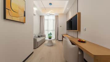 Een moderne hotelkamer met een houten bureau, een flatscreen televisie, een ronde salontafel en een bank.