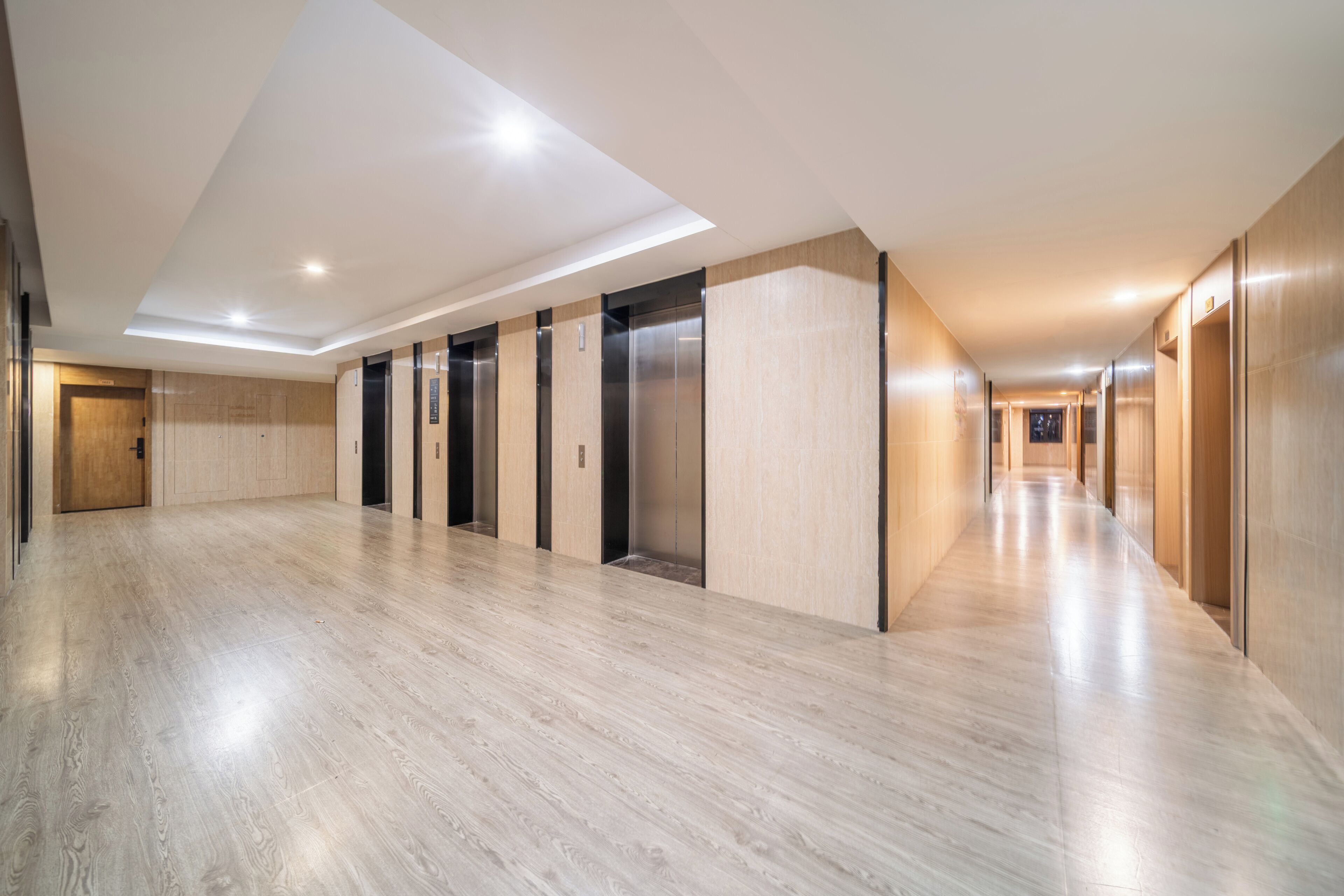 A long, well-lit hallway with wooden flooring and multiple elevators.