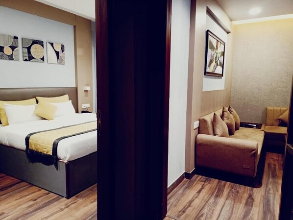 A hotel room with a bed, a sofa, and a small table. - Western Blu (New Delhi)