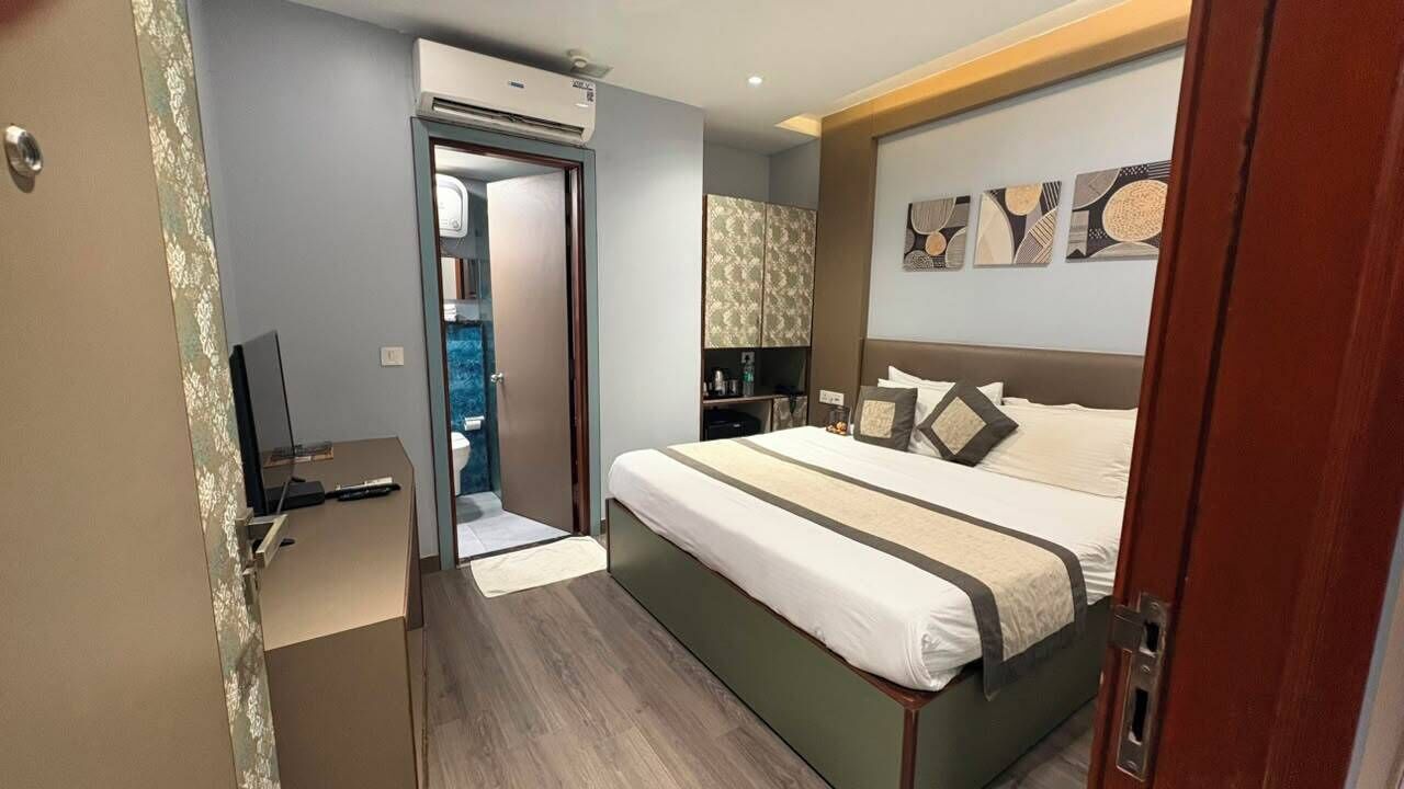Ett hotellrum med en säng, ett sängbord, en spegel och en dörr som leder till ett badrum.