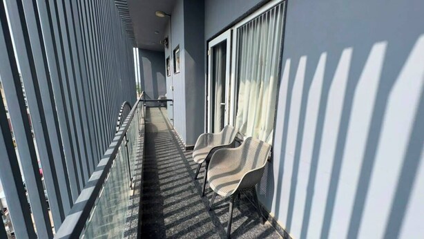 Un pasillo con sillas, barandilla de vidrio y una puerta con cortinas.