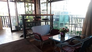 Una stanza con una porta in vetro che dà su un balcone, un divano, un tavolo con sedie e una pianta in vaso.