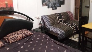 Una camera da letto con un letto, una poltrona, una sedia, un tavolino e una parete decorata con un'opera d'arte che raffigura un paesaggio urbano.
