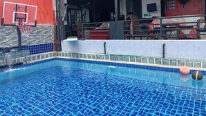 A swimming pool with a basketball hoop, a covered seating area, and a red wall. - Room-cozy Deluxe Guest Room in South Pat (Pattaya)