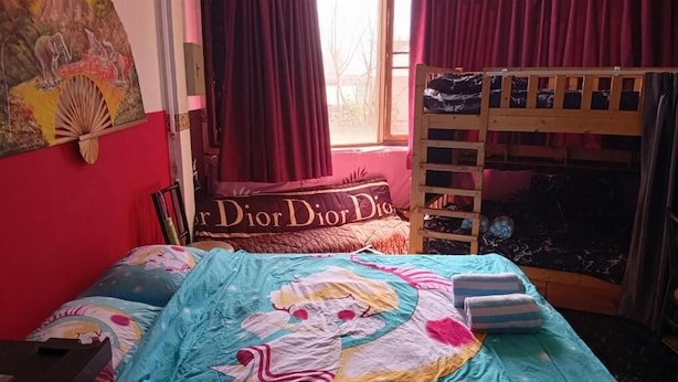 Ein Schlafzimmer mit einem Etagenbett, einem Bett mit farbenfroher Decke, einer roten Wand und einem Fenster mit Vorhängen.