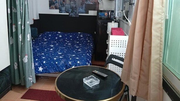 Ein Schlafzimmer mit einem Bett, einem kleinen Tisch, einem Ventilator, einer Heizung und einem an der Wand befestigten Fernseher.