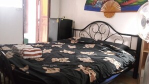 Una habitación con cama, ventilador, un cuadro en la pared y una puerta que da al exterior.