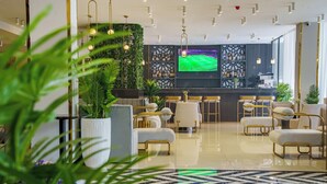 Un moderno vestíbulo de hotel con una zona de bar, asientos y una gran pantalla mostrando un evento deportivo.