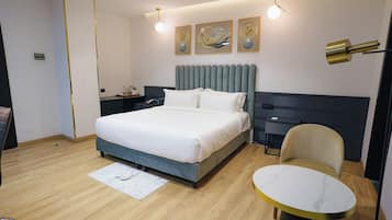A modern hotel room with a large bed, bedside tables, a desk, a chair, and a round table.