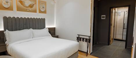 A modern bedroom with a large bed, a bedside table, a wall-mounted light fixture, and a door leading to a bathroom.