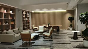 A modern living room with a sofa, chairs, a coffee table, a dining area with a table and chairs, and a bookshelf filled with books and decorative items. - Poltton International Service Apartment (Liuzhou Yaobu Ancient Town Chengzhong Wanda Plaza) (Liuzhou)