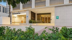 Entrada de un edificio moderno con fachada de vidrio, un hidrante visible y un letrero que indica un área de estacionamiento.