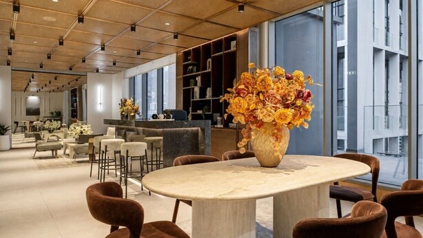 Un interior moderno con una mesa redonda, sillas y un jarrón grande lleno de flores.