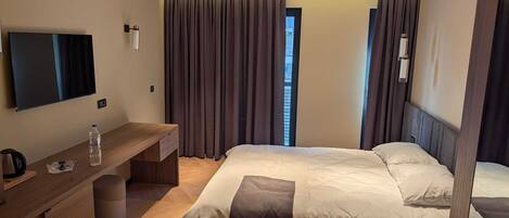 A hotel room with a bed, a desk with a chair, a television, and a window with curtains.
