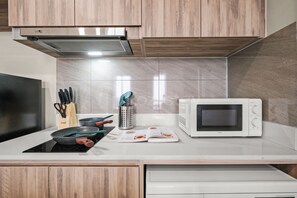 A modern kitchen with wooden cabinets, a stainless steel range hood, a microwave, and a stovetop. - Romel by Kozystay - Kemayoran (Jakarta)