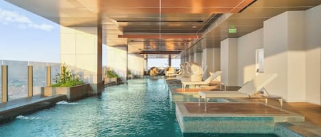 Uma piscina infinita interior com espreguiçadeiras e vista para a cidade.