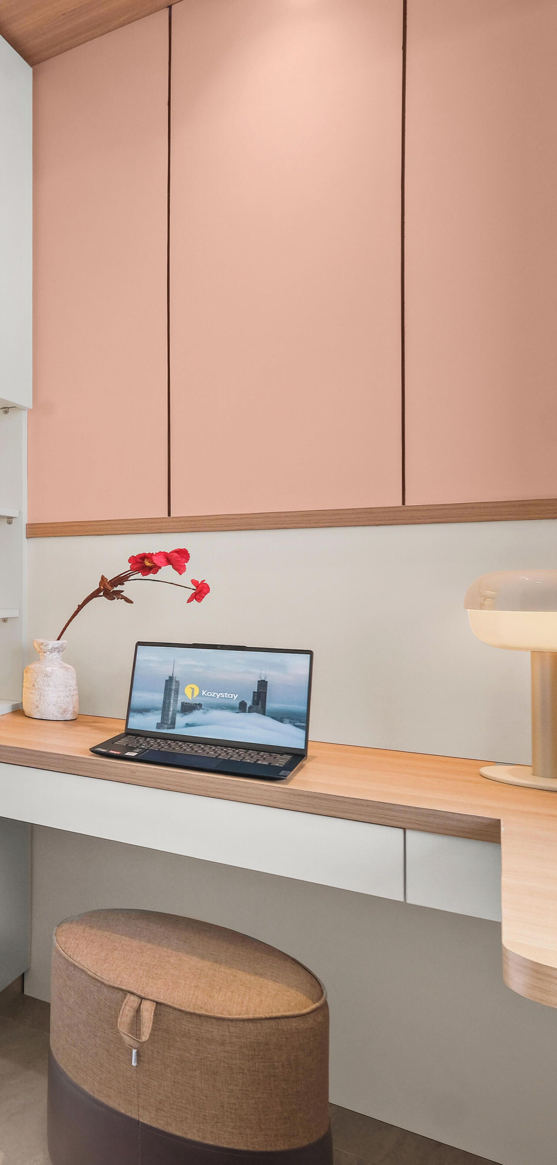 Un espacio de trabajo moderno con una computadora portátil sobre un escritorio de madera, un florero con flores rojas y un otoman redonda.