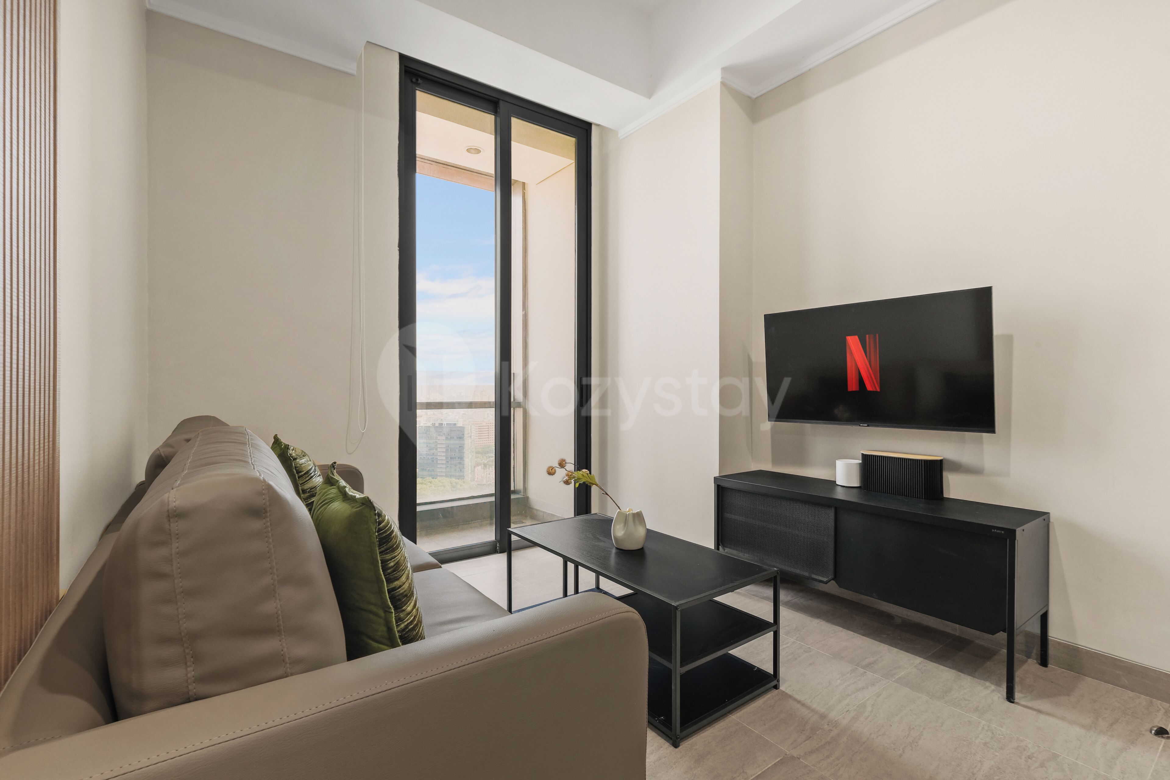 A modern living room with a sofa, a coffee table, a TV, and a balcony with a city view.