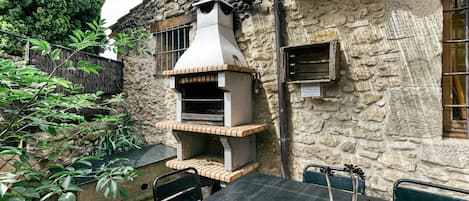 Un patio al aire libre con pared de piedra, horno de ladrillo, mesa con sillas y planta en maceta.