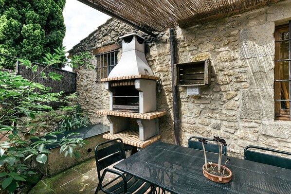 An outdoor patio with a stone wall, a brick oven, a table with chairs, and a potted plant.