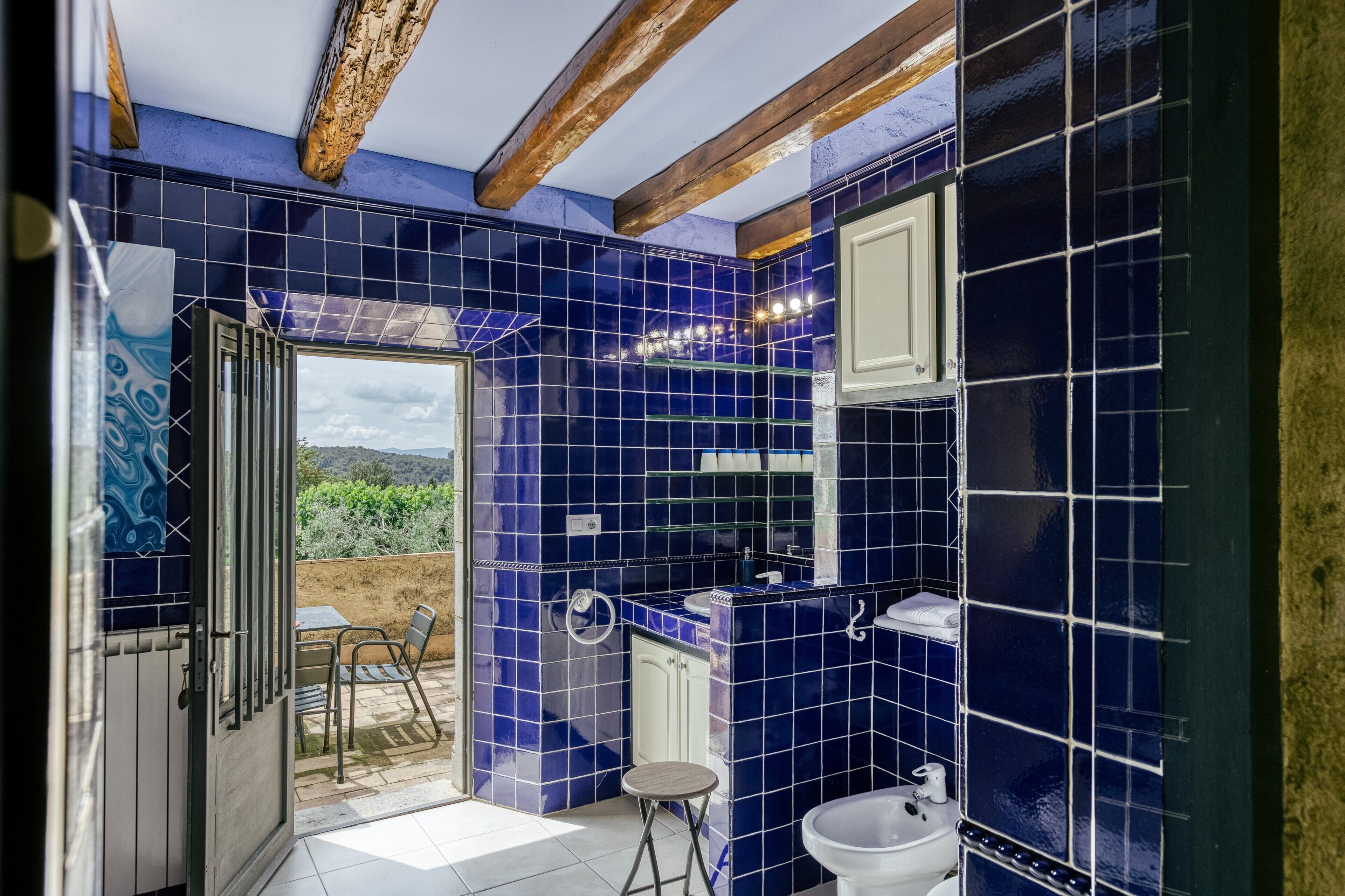 Un baño con azulejos azules, un lavamanos blanco y un taburete pequeño.