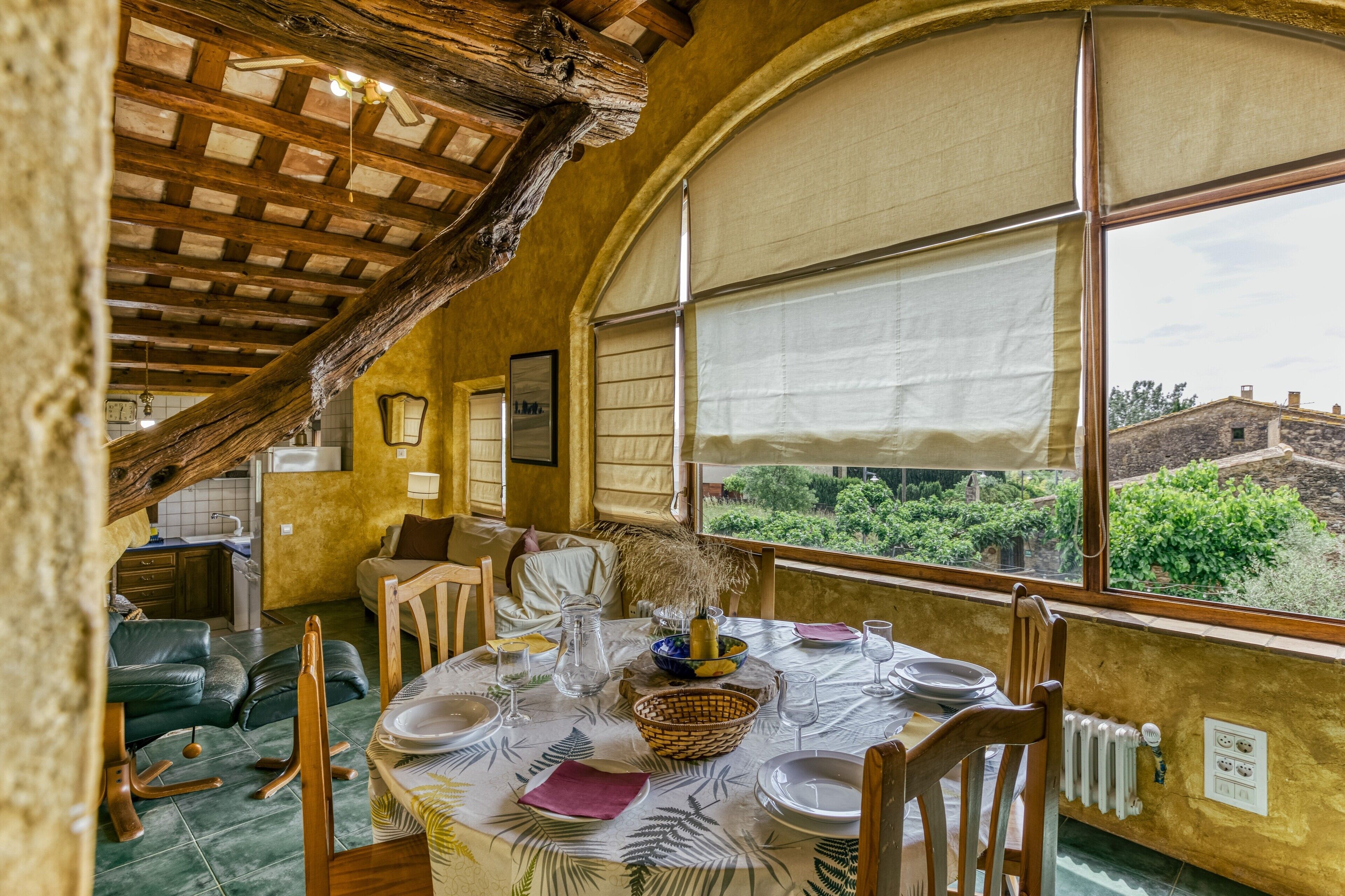 A dining area with a table set for four, a view of the outdoors through large windows, and a rustic wooden ceiling.